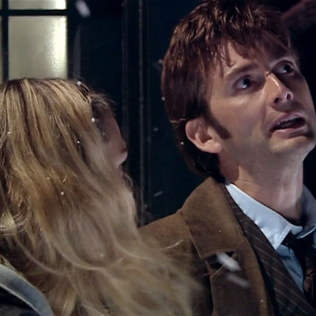 The Tenth Doctor (David Tennant) is looking upwards towards thee sky Rose Tyler (Billie Piper) is turned towards him
