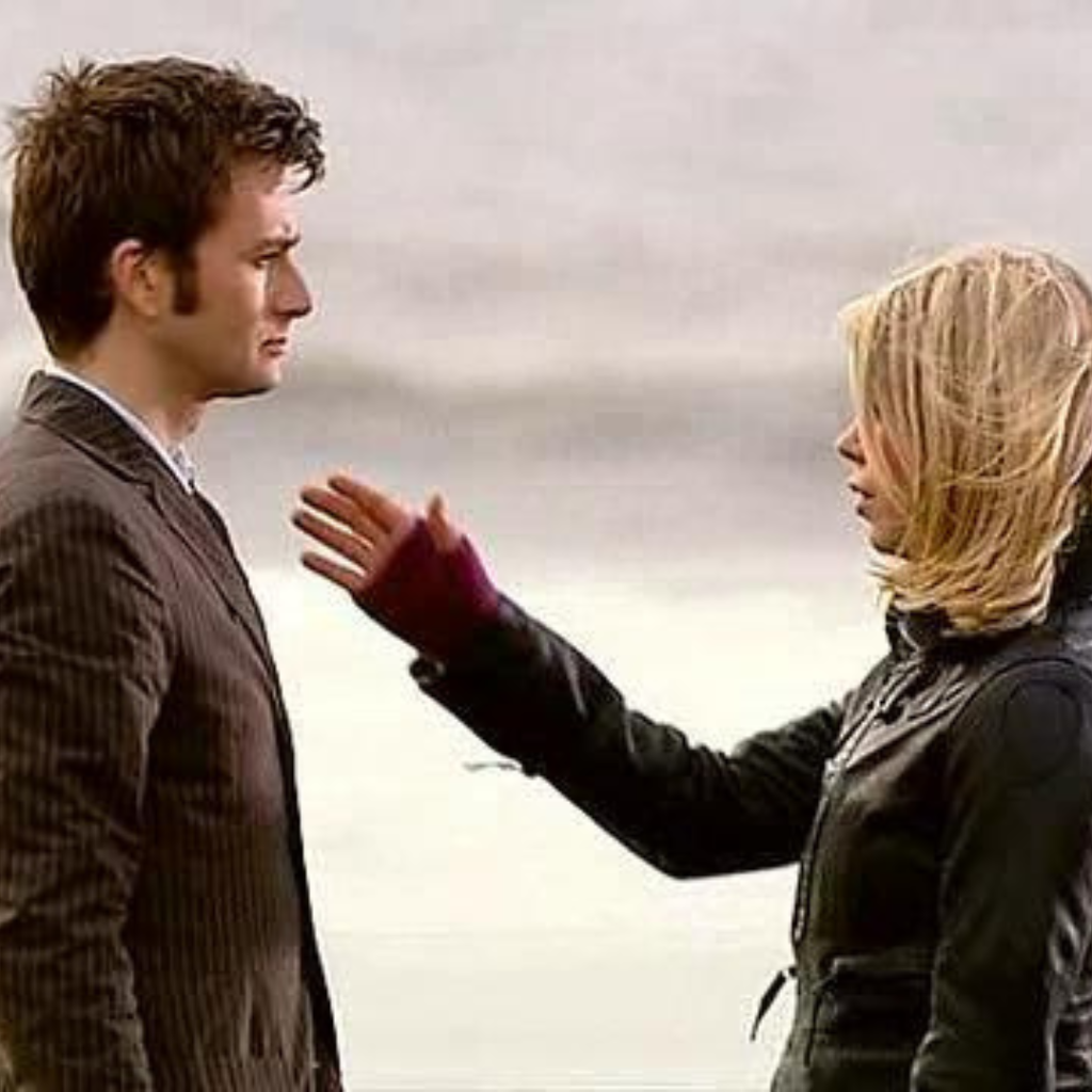 The Tenth Doctor (David Tennant) faces Rose Tyler (Billie Piper) who has her arm outstretched on a beach