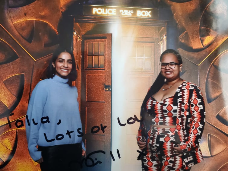 A photo of Talia and Mandip Gill in front of a green screen Tardis from Gallifrey One in 2022. It's signed "Talia, Lot's of love" followed by Mandip Gill's signature